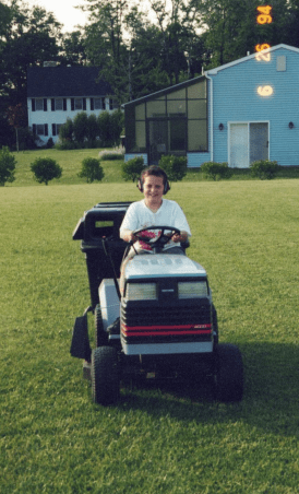 Young boy riding toy car on lawn