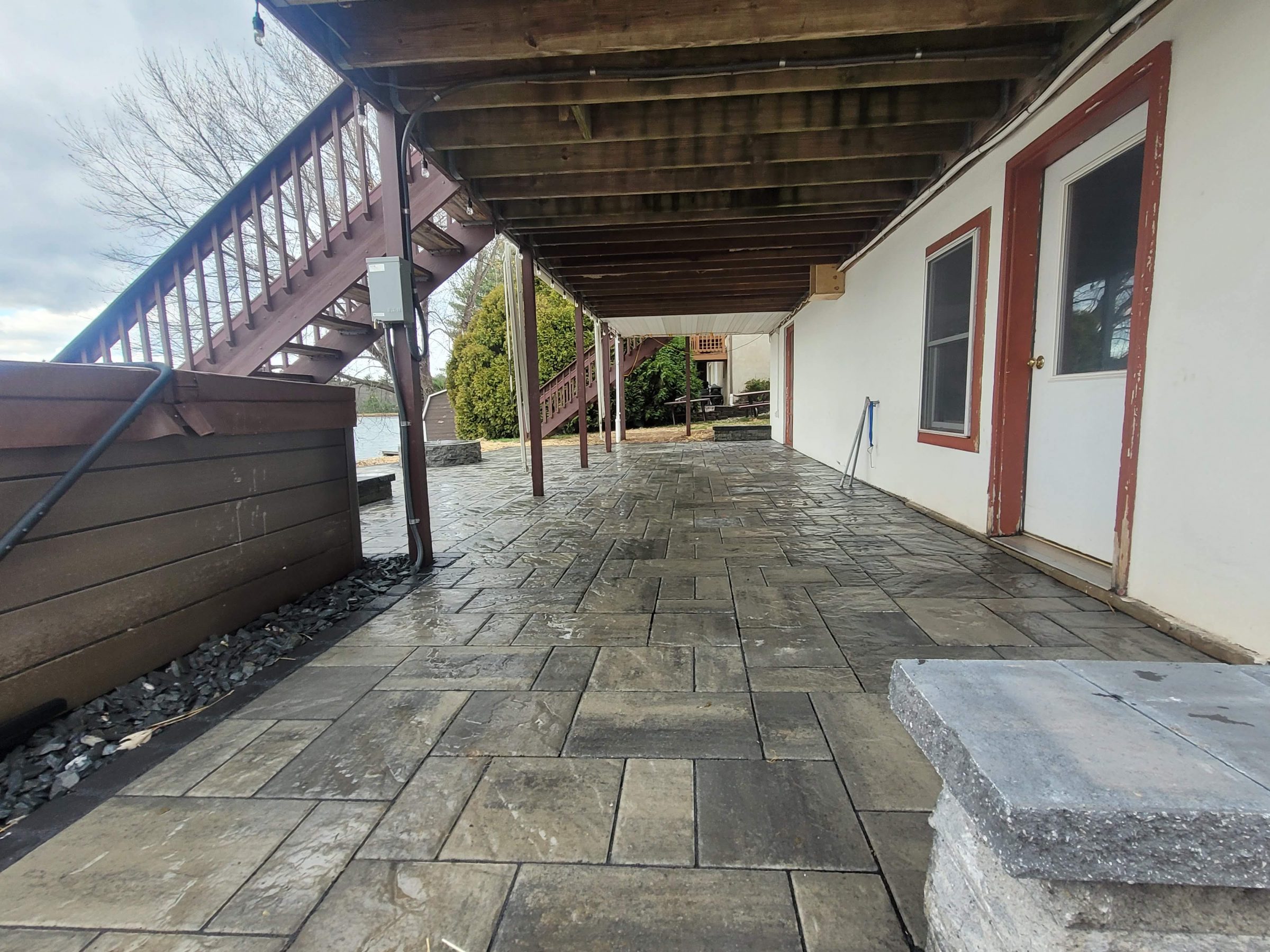 Covered stone patio beneath wooden deck and stairs